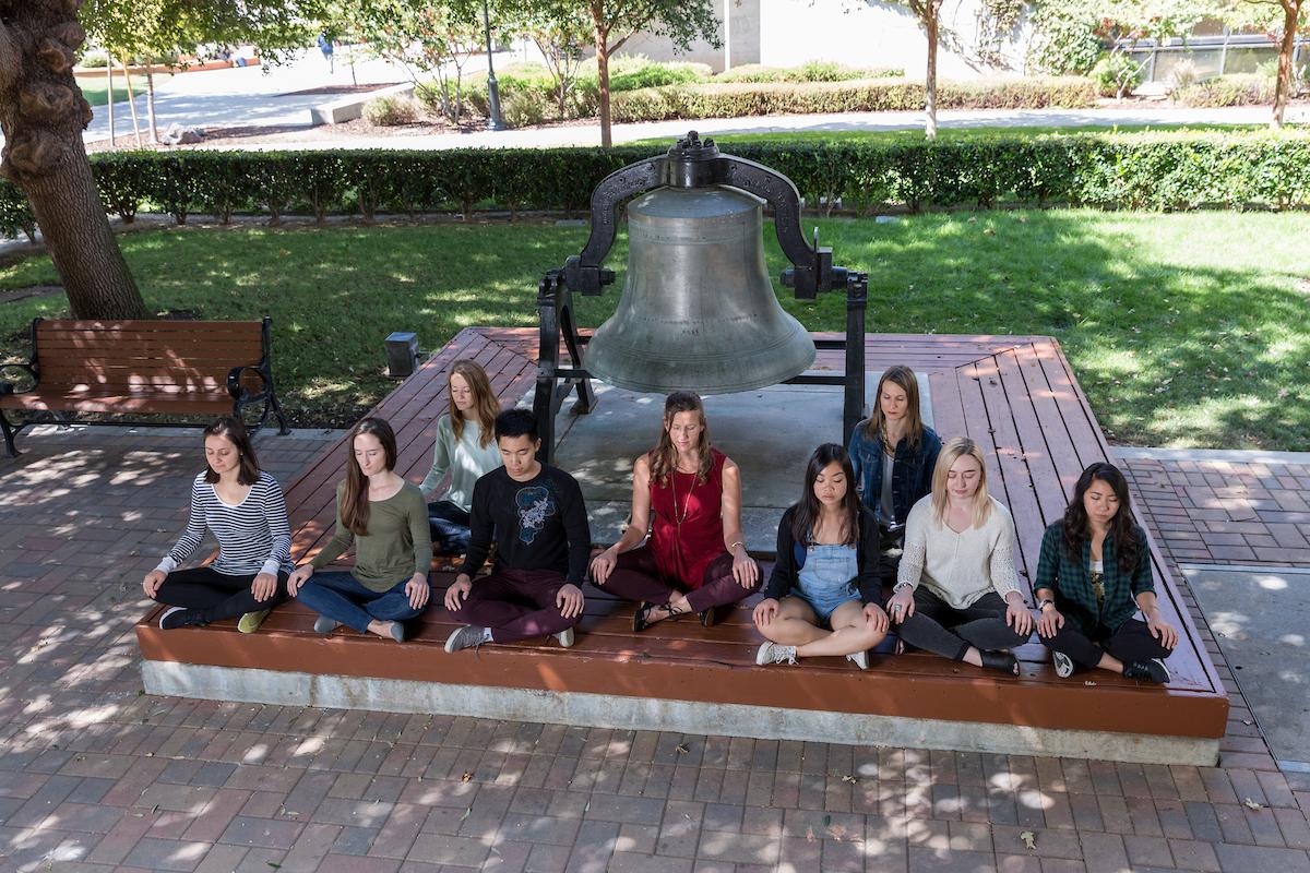 students meditating outside with a bell